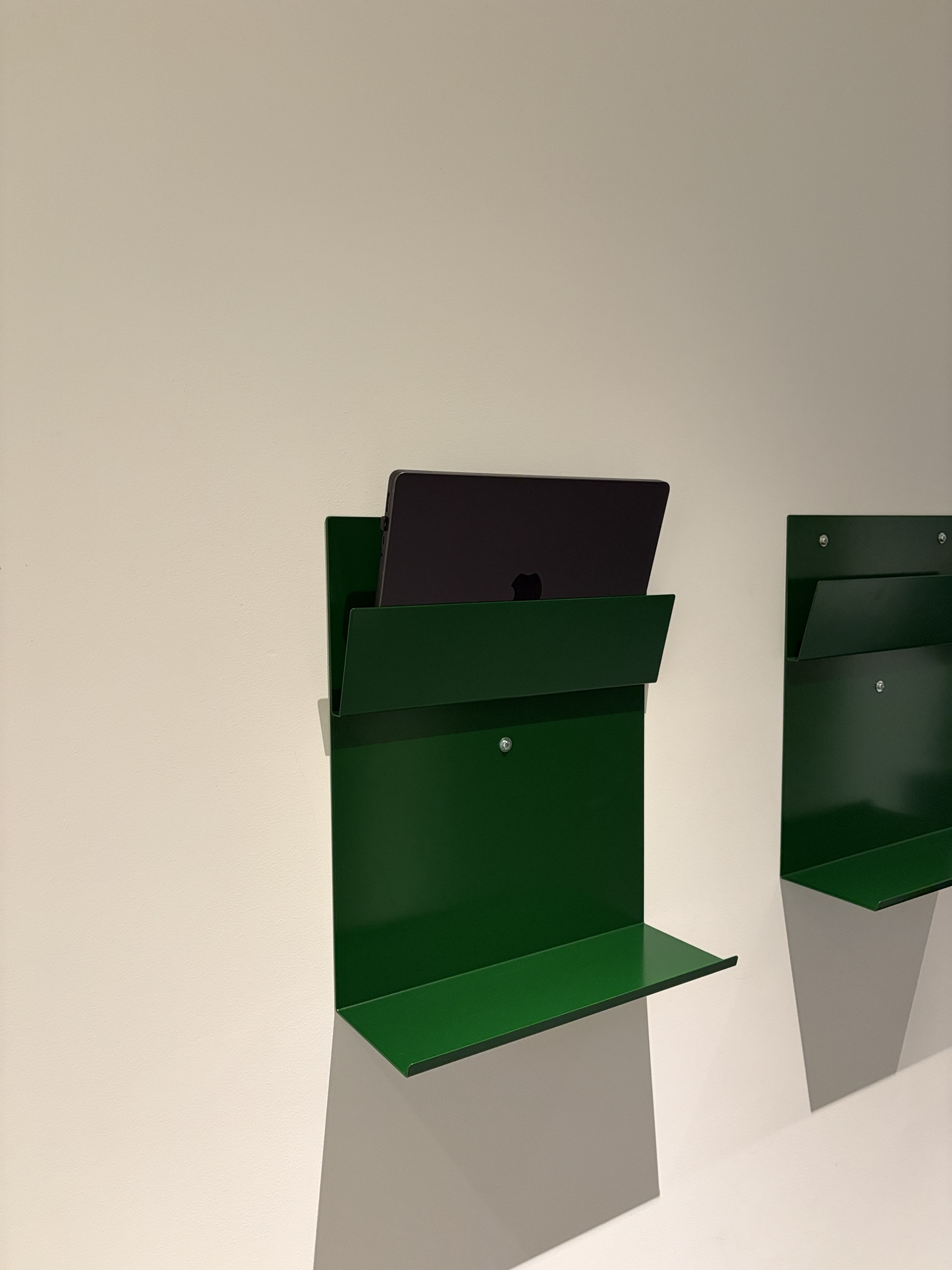 Green folded steel wall shelf holding a laptop